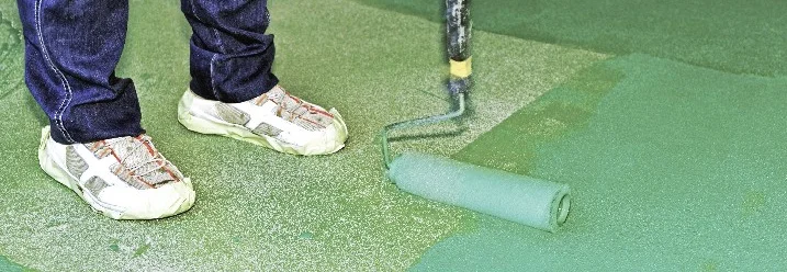 Person streicht Boden grün mit Farbrolle